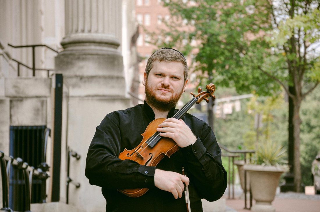 Dr. Yonatan Grinberg holding his violin outdoors